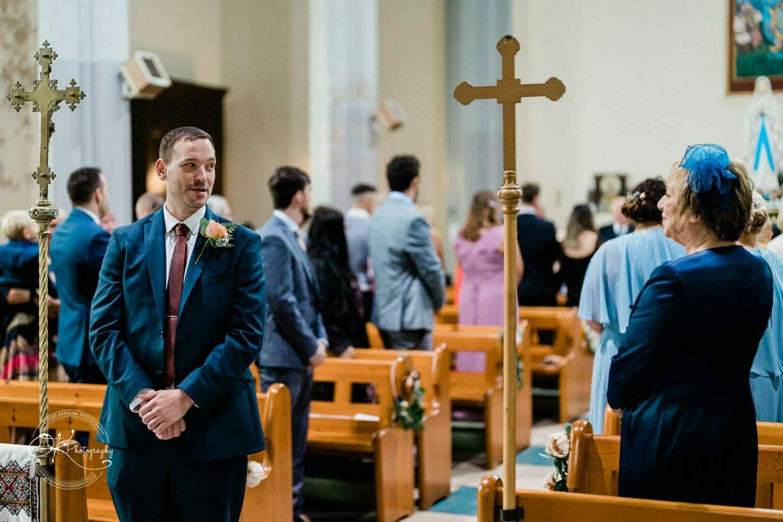 Wedding photography The Embankment A man in a suit and a woman in a blue dress attend a church ceremony, surrounded by guests seated in wooden pews.