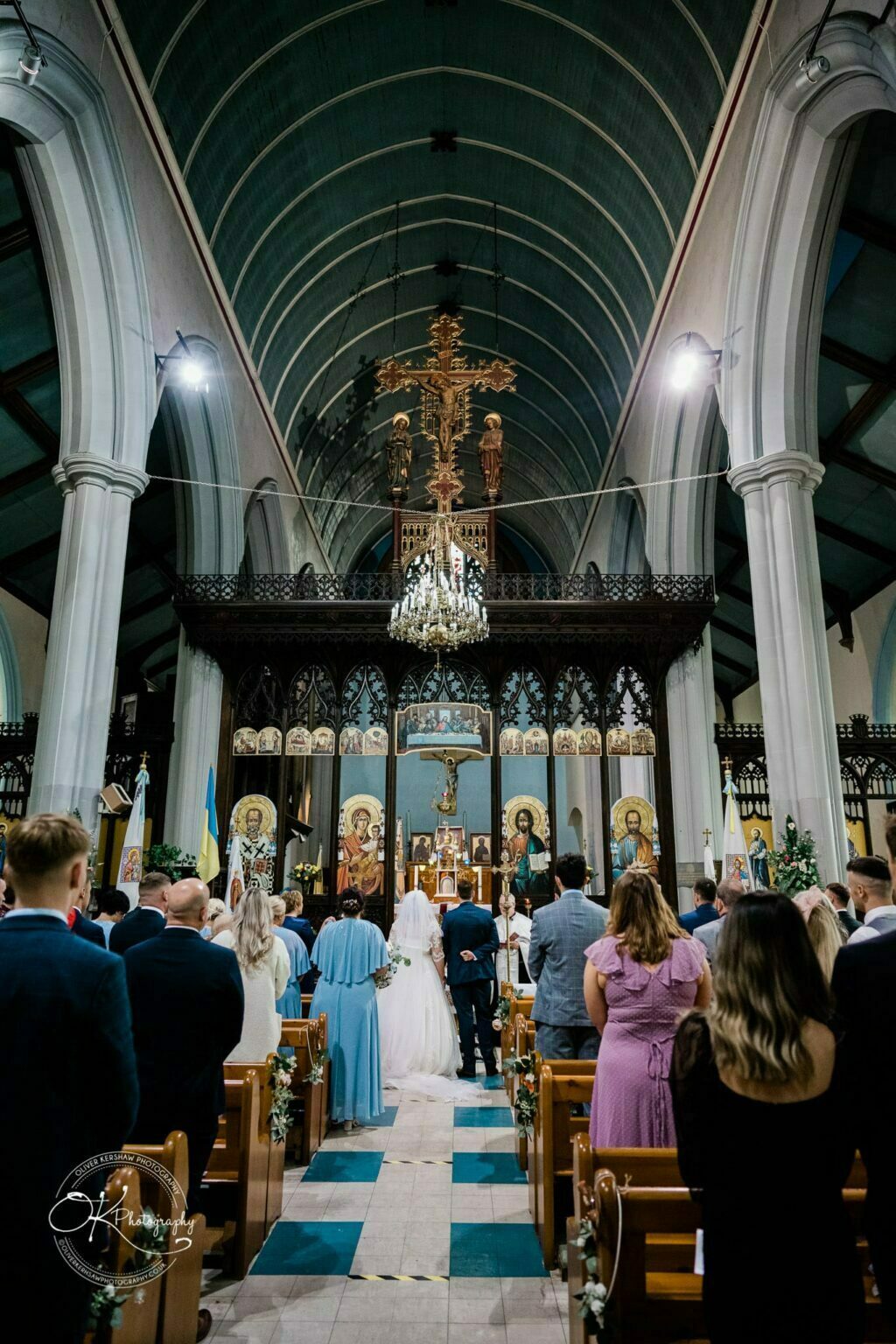 Wedding photography The Embankment Interior of a church with people attending a wedding ceremony, featuring high arched ceilings and religious icons on the altar.