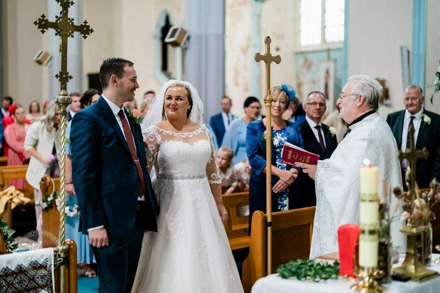 Wedding photography The Embankment A bride and groom stand at the altar during their wedding ceremony in a church, with a priest officiating and guests seated in the background.