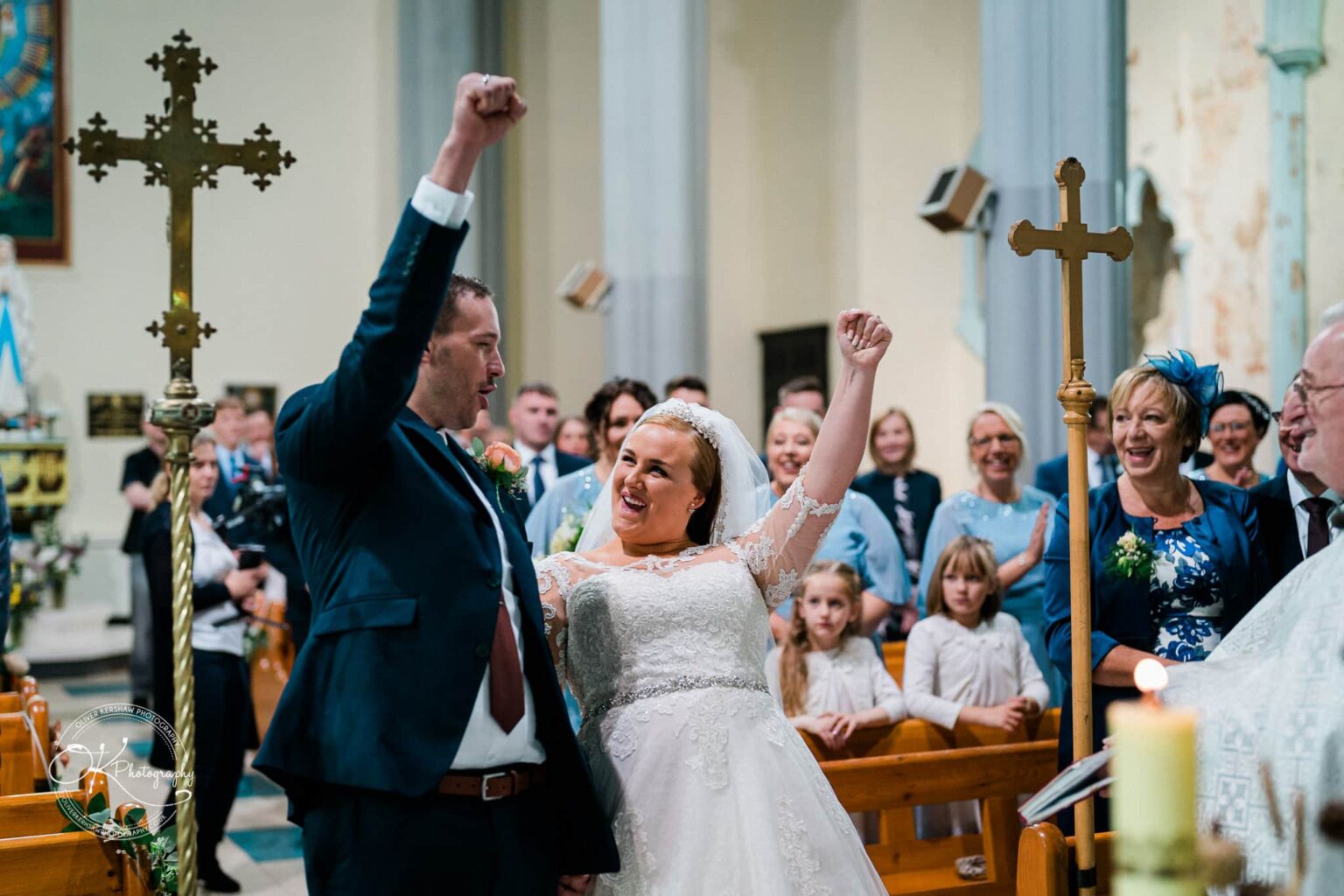 Wedding photography The Embankment A newlywed couple is celebrating with raised fists in a church, surrounded by joyful guests.