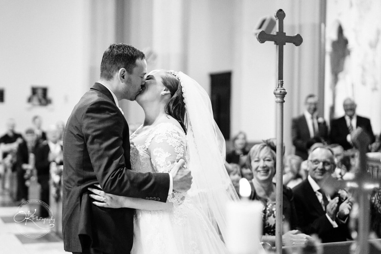 Wedding photography The Embankment A bride and groom kissing in a church during their wedding ceremony, with guests smiling and clapping in the background.