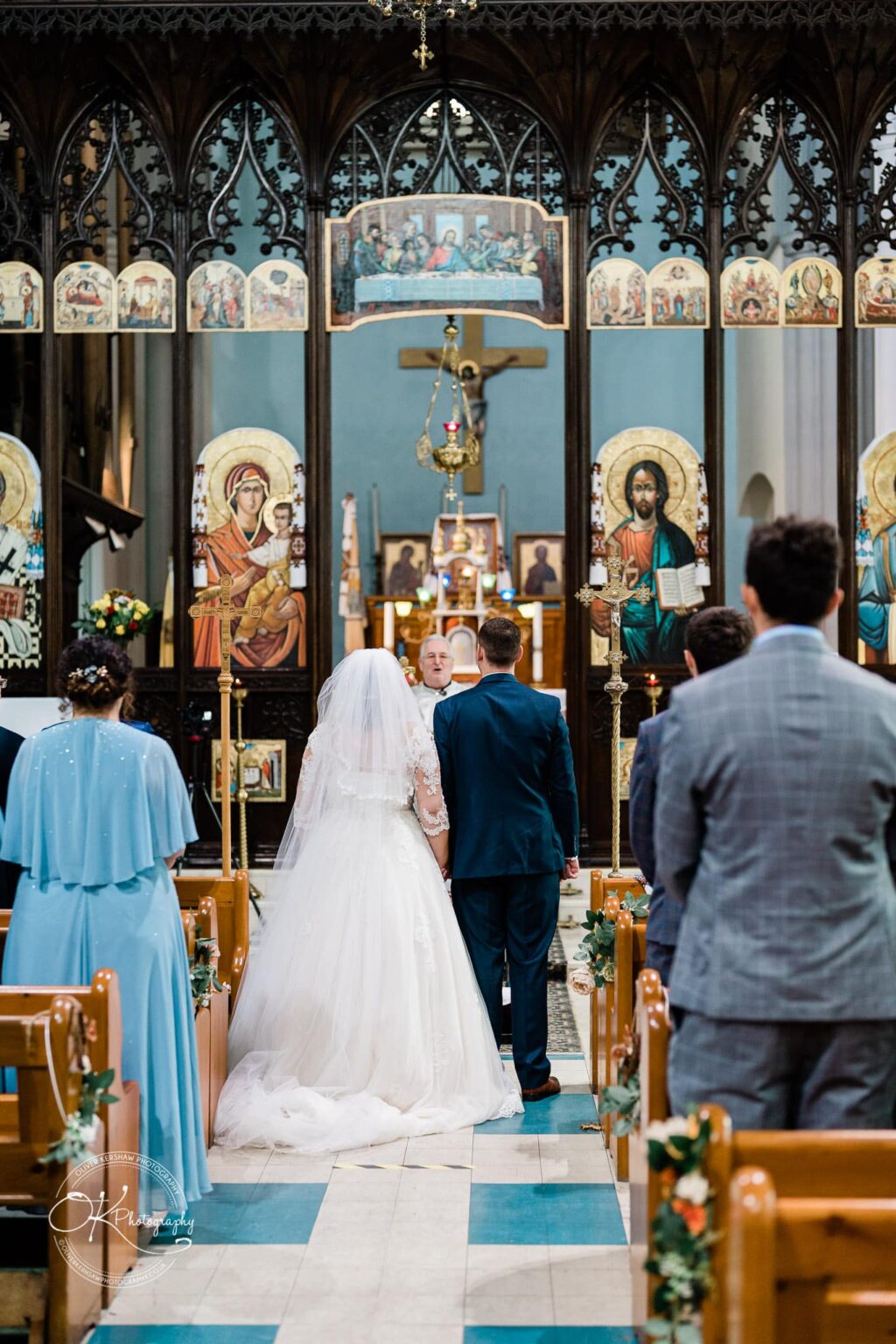Wedding photography The Embankment Bride and groom standing at the altar of an ornate church during their wedding ceremony, surrounded by guests.