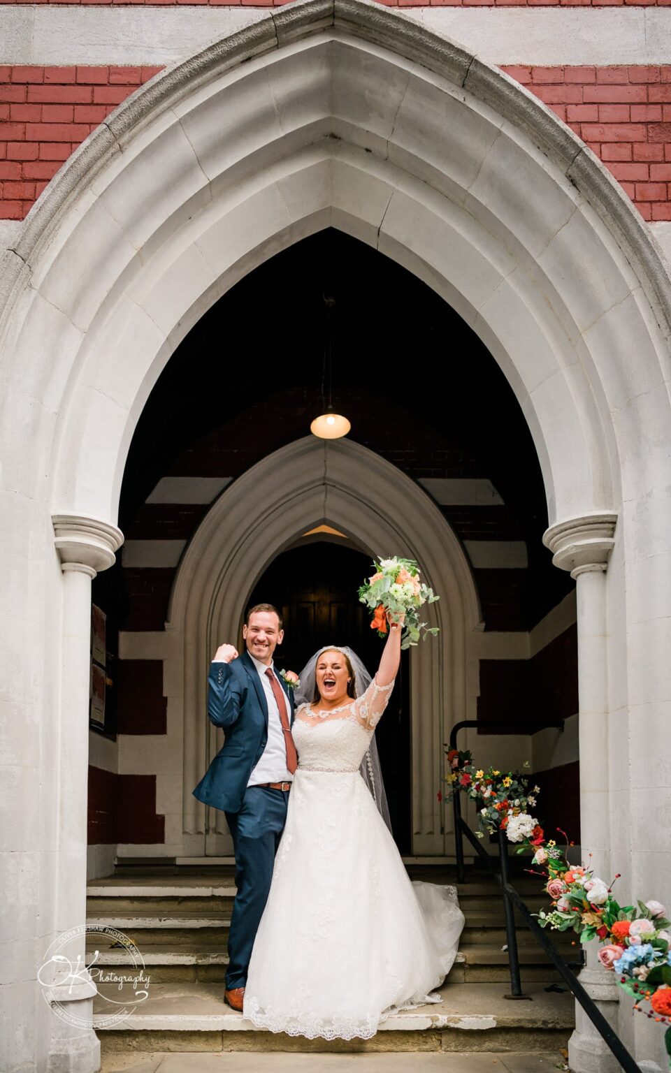 Wedding photography The Embankment A bride and groom cheerfully celebrating while standing on the steps of a church entrance adorned with flower arrangements.