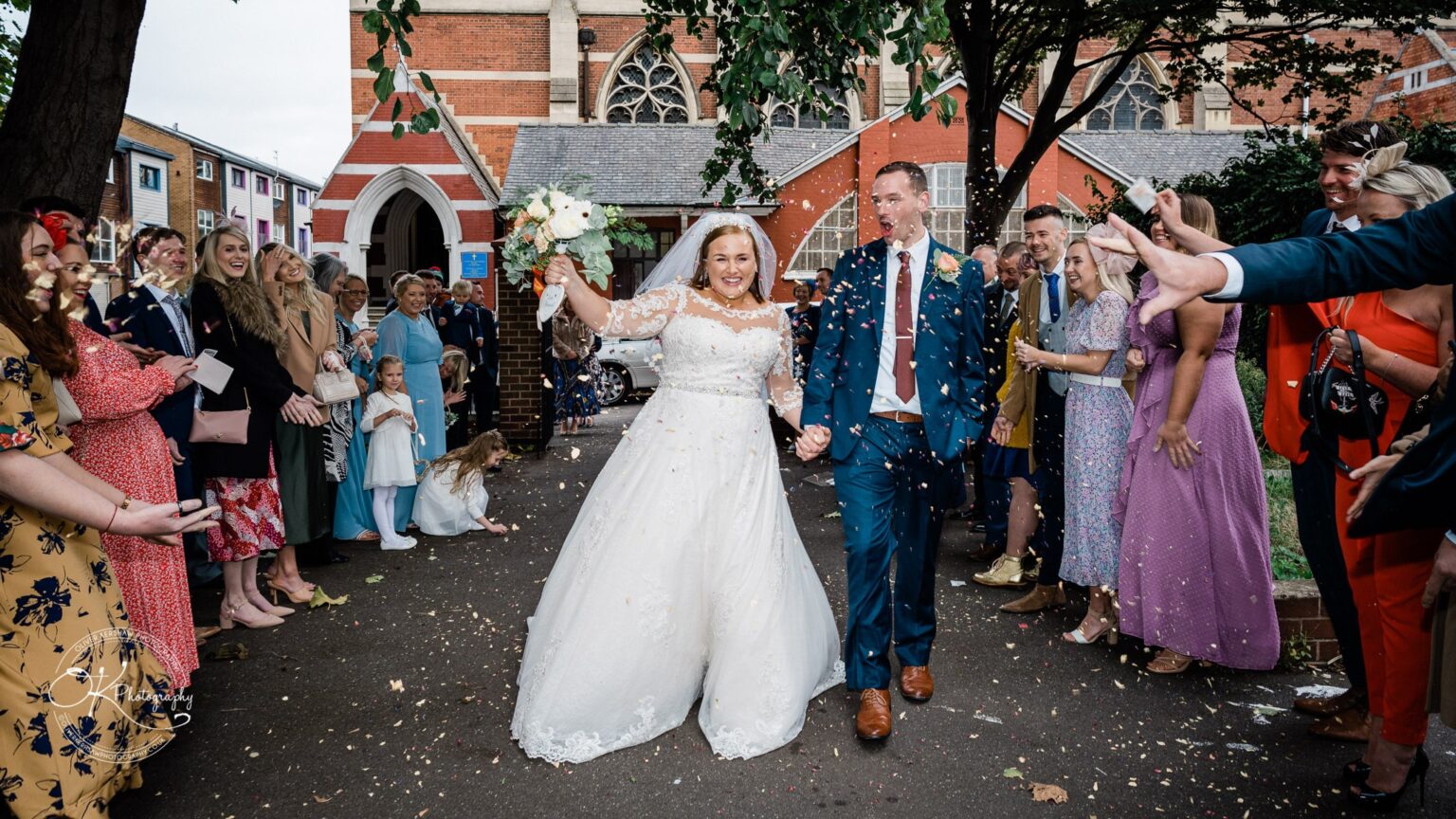 Wedding photography The Embankment Newlywed couple walking outside a church, surrounded by guests throwing confetti.
