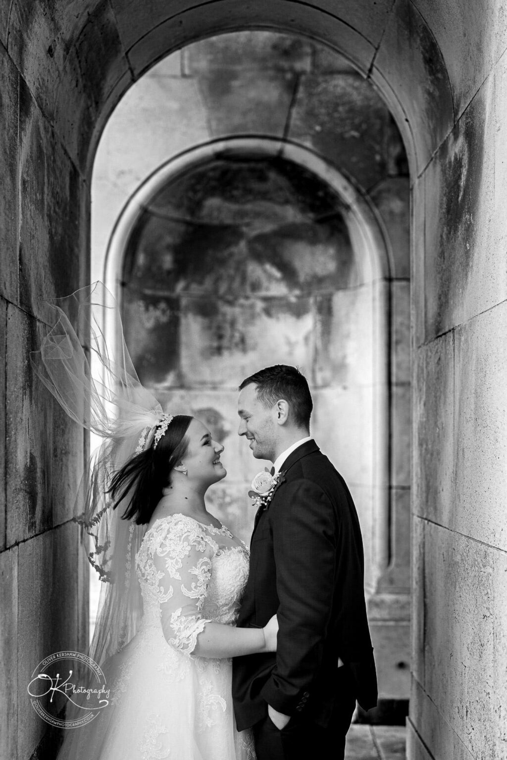 Wedding photography The Embankment A newlywed couple standing face-to-face under a stone archway, with the bride's veil blowing in the wind.