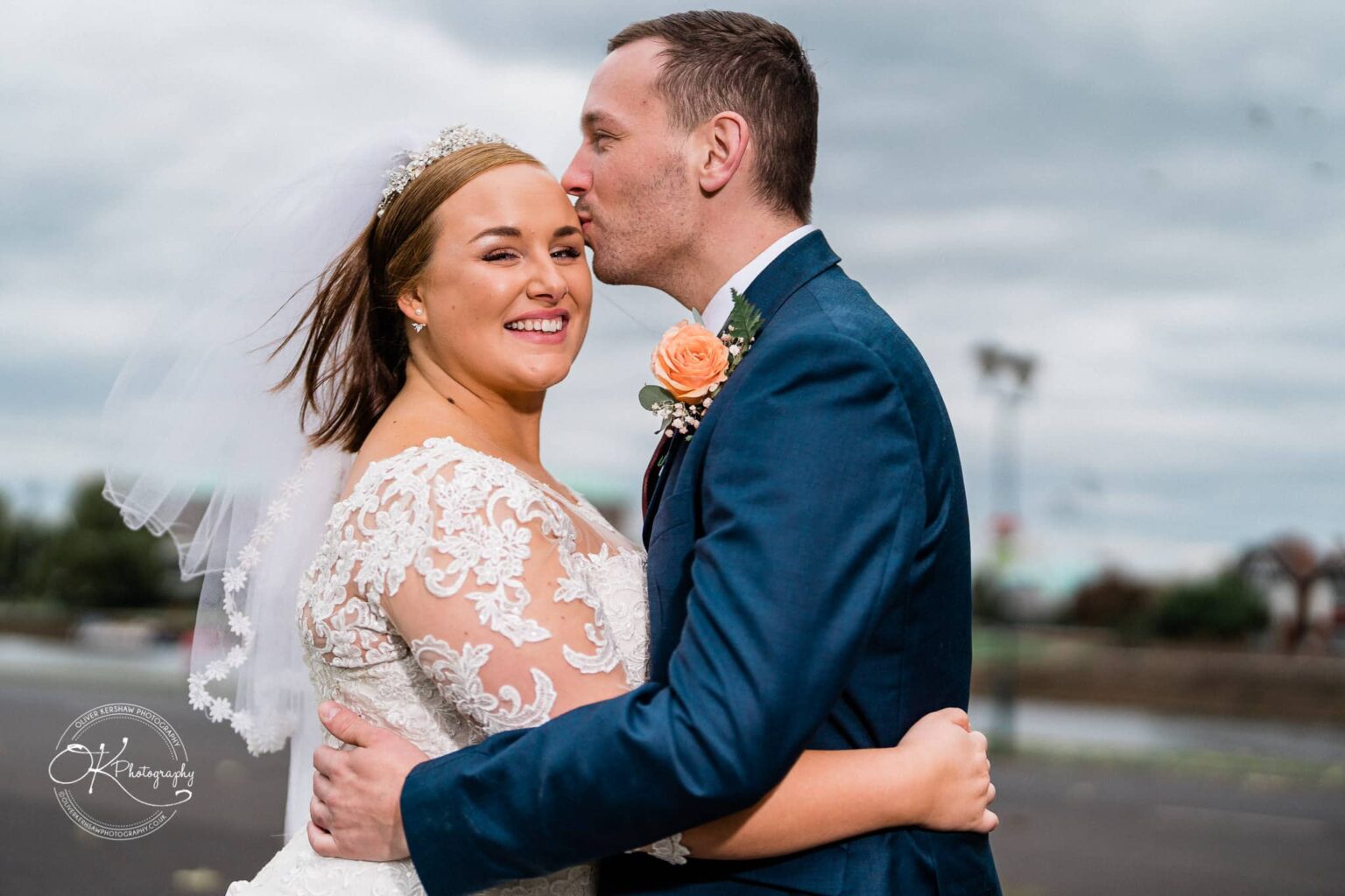 Wedding photography The Embankment A bride and groom embrace outdoors, the groom kisses the bride's forehead while she smiles at the camera.