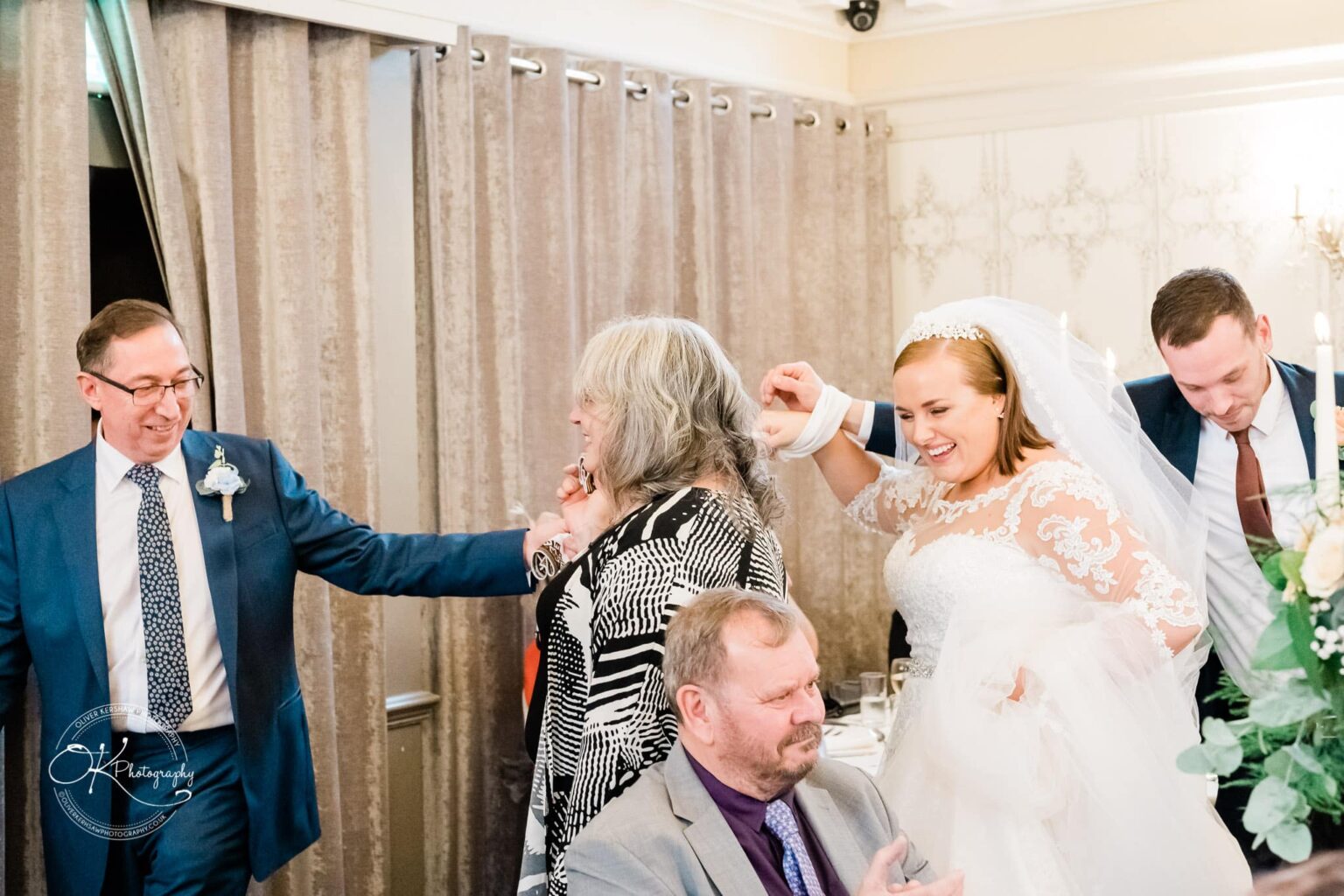 Wedding photography The Embankment A wedding celebration with four people interacting; a bride in a white gown is smiling, along with three men in suits and a woman with grey hair.
