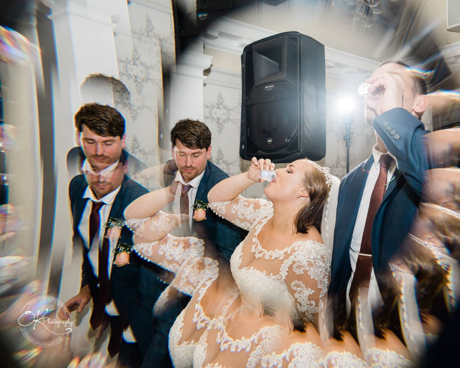Wedding photography The Embankment A bride in a lace wedding dress and three men in suits taking shots at a wedding reception with a kaleidoscopic effect.