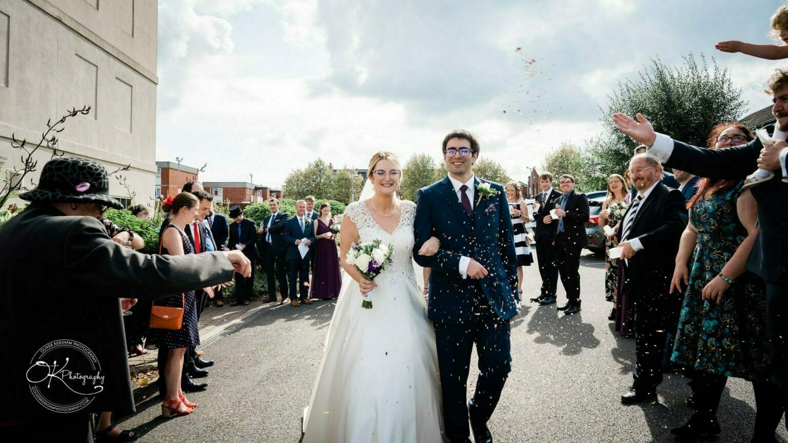Yew Lodge Hotel Wedding Photography Bride and groom smiling while walking through a confetti shower, surrounded by wedding guests.