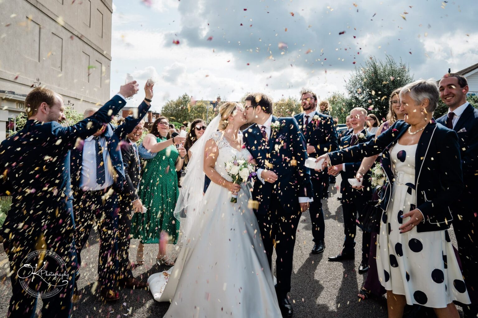 Yew Lodge Hotel Wedding Photography Newlywed couple kissing while guests throw confetti at an outdoor wedding ceremony at Yew Lodge Hotel.