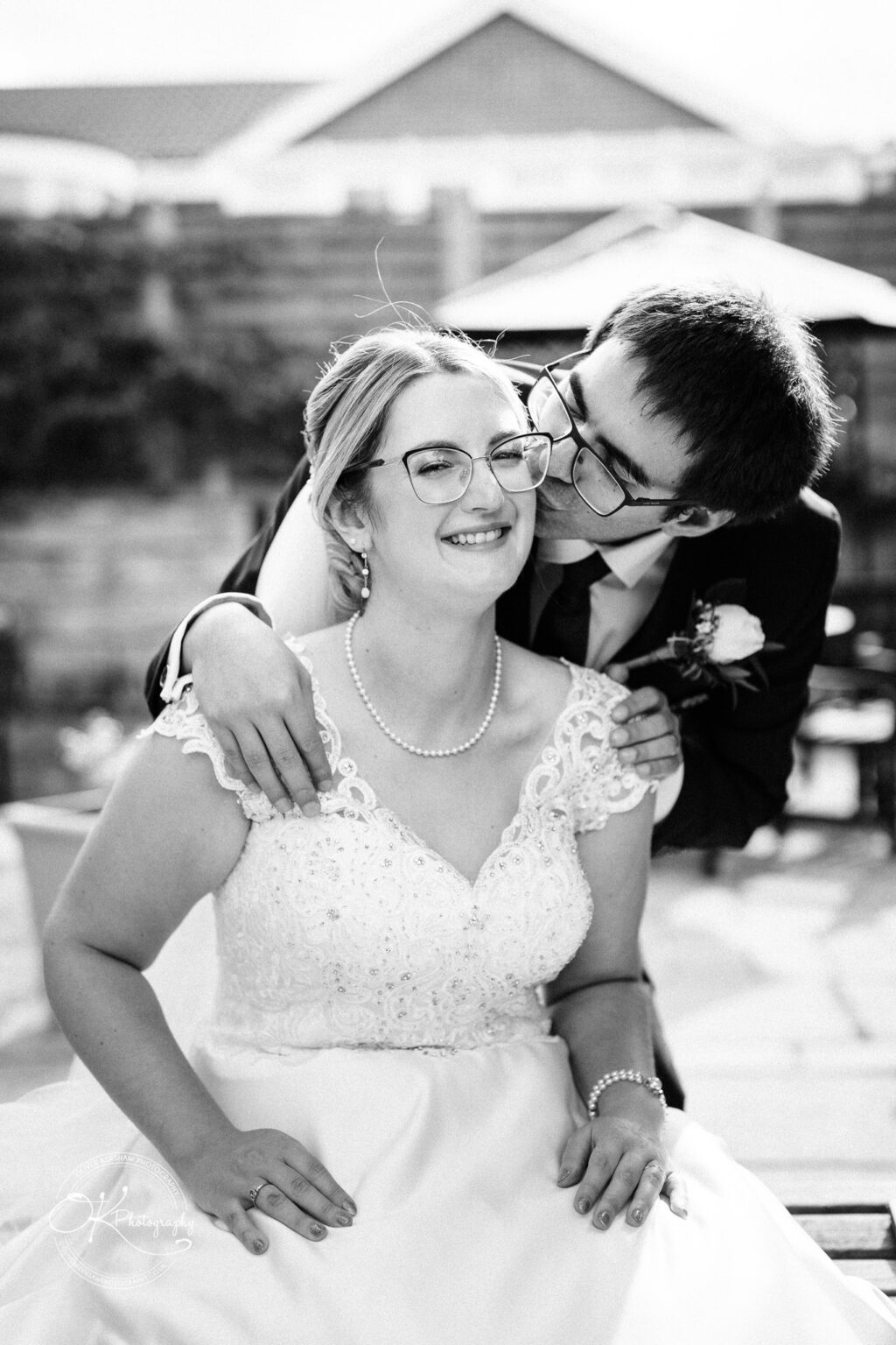 Yew Lodge Hotel Wedding Photography Bride and groom in wedding attire, the groom gently kissing the bride's cheek, both wearing glasses, in a black and white photo.