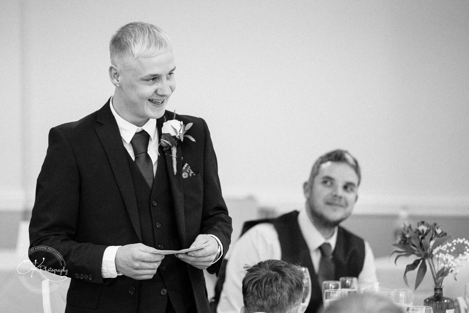 Yew Lodge Hotel Wedding Photography Best man giving a speech at a wedding reception, with a groomsman in the background.
