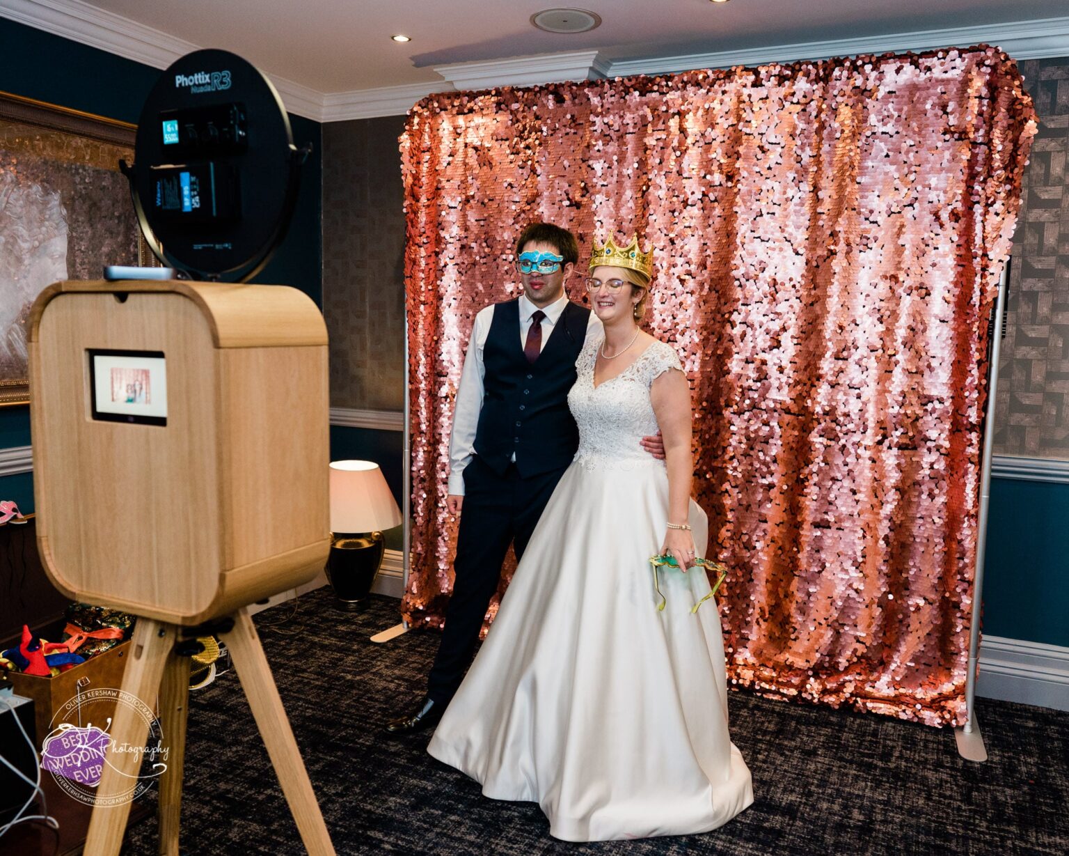 Yew Lodge Hotel Wedding Photography Bride and groom posing in front of a photo booth with a pink sequin backdrop, wearing fun accessories.