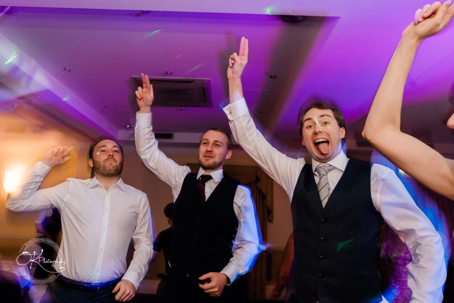 Yew Lodge Hotel Wedding Photography Three men in formal attire dancing and celebrating at a wedding reception.