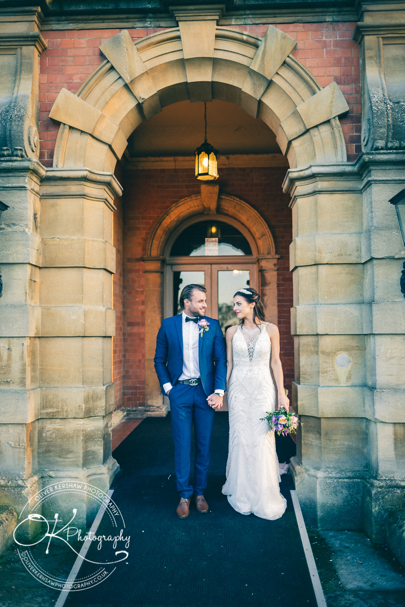 Bride and groom holding hands and walking out of a historic brick building with an arched entrance.