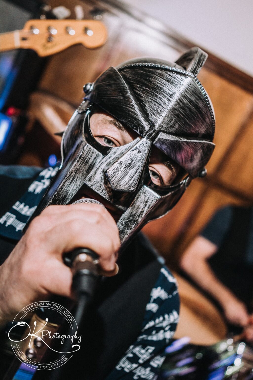 Wedding Photography George Hotel Stamford Man wearing a metal mask holding a microphone with blurred musical instruments in the background.