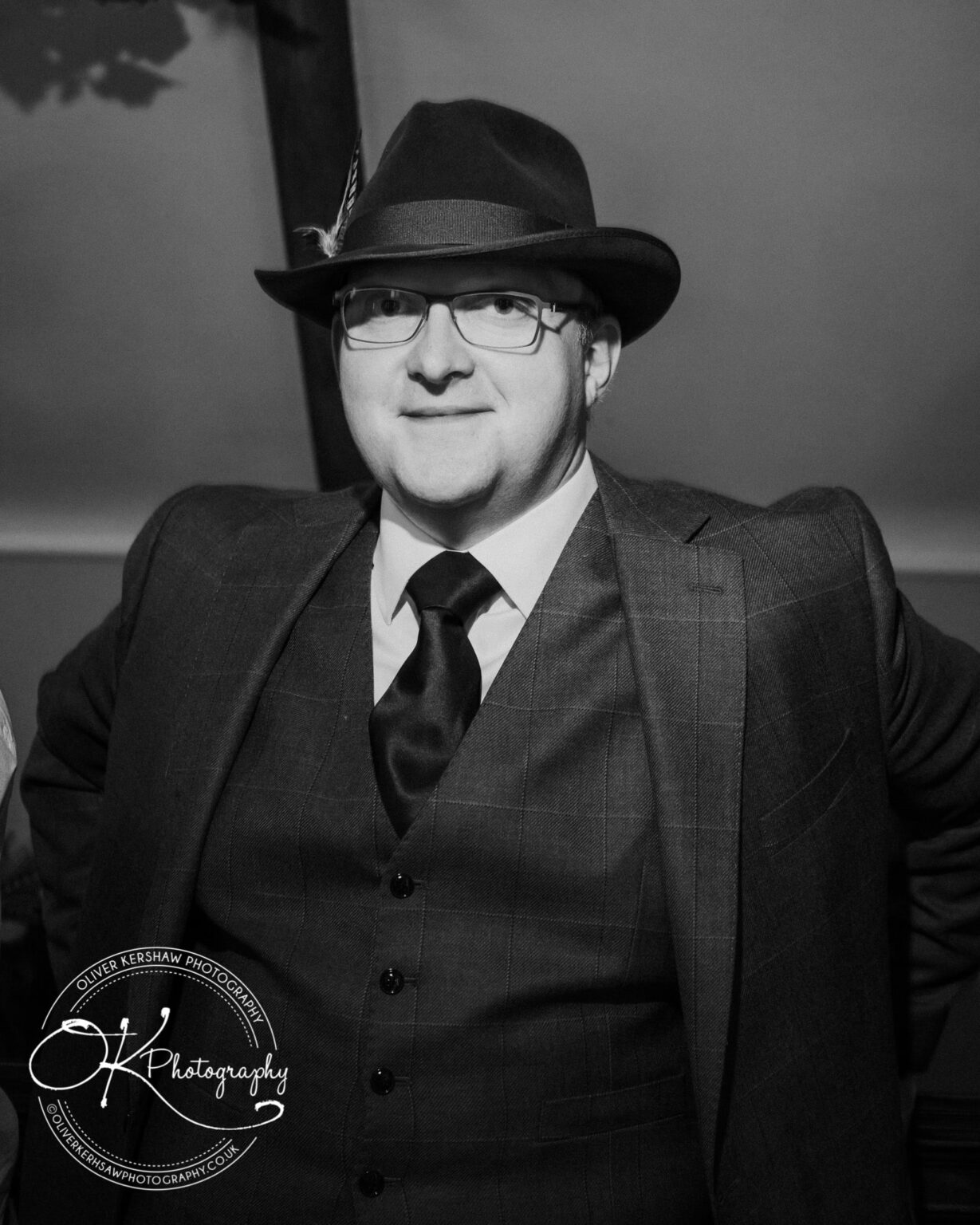 Wedding Photography George Hotel Stamford A man wearing a hat, glasses, and a three-piece suit, smiling and posing for a photograph.