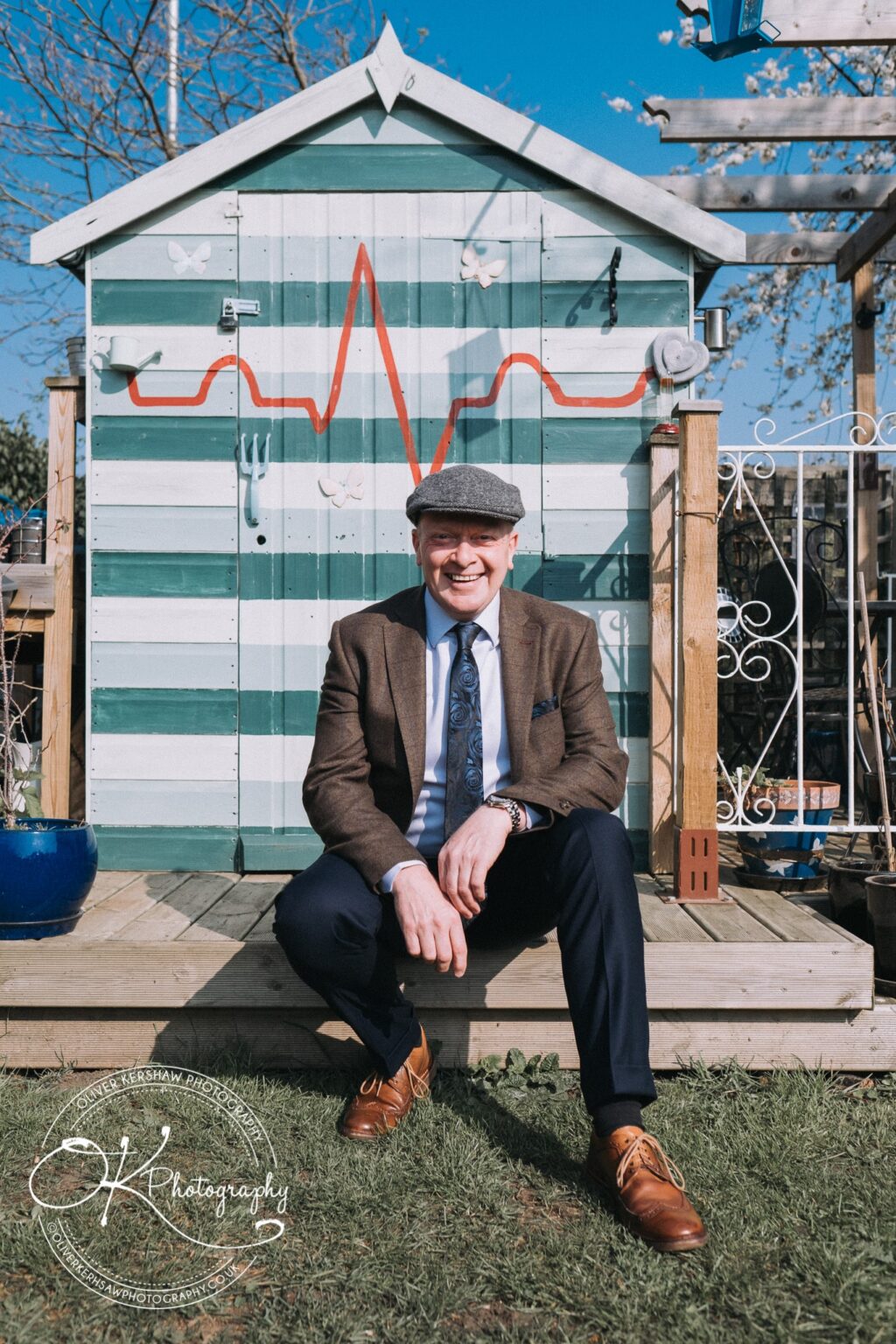 Wedding Photography George Hotel Stamford A man in a flat cap and suit sitting on steps in front of a striped shed with an ECG line painted on it.