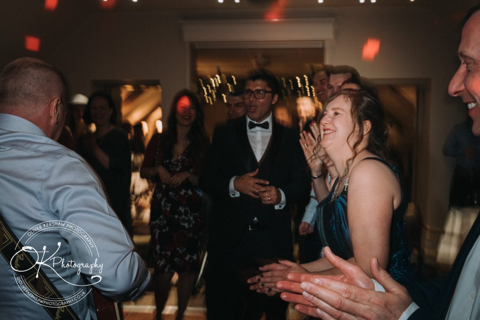 Wedding Photography George Hotel Stamford People dancing and smiling at an indoor social event with mood lighting, featuring a guitarist in the foreground.