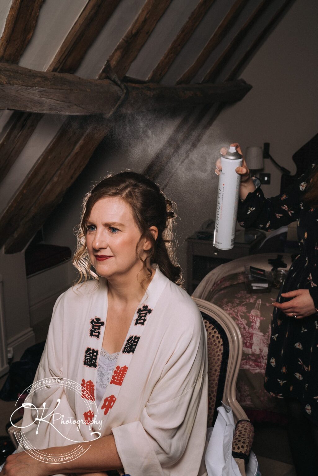 Wedding Photography George Hotel Stamford A woman having her hair styled with hairspray in a rustic room with wooden beams.