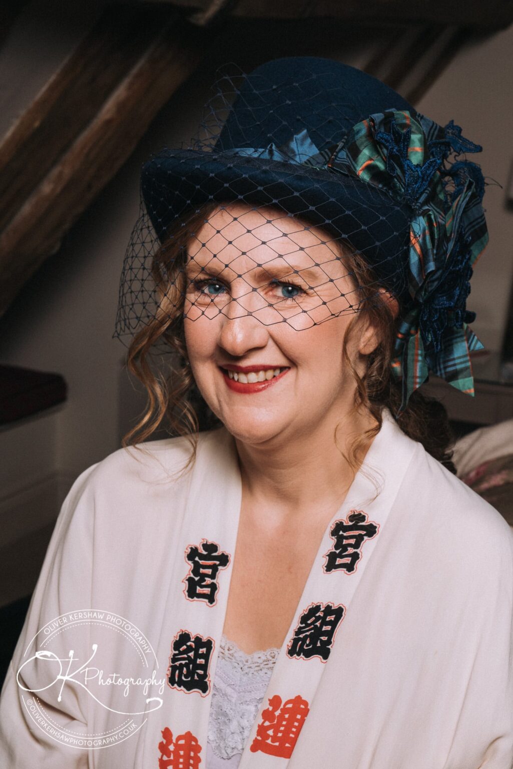 Wedding Photography George Hotel Stamford A person dressed in vintage attire, including a blue hat with a netted veil and decorative ribbon, smiling indoors.