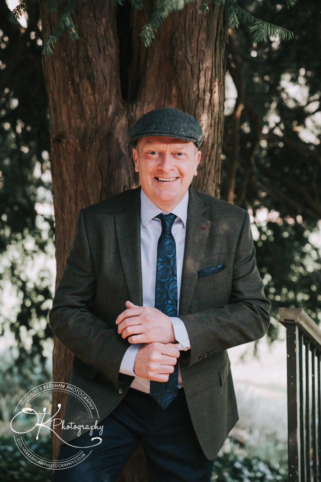 Wedding Photography George Hotel Stamford Man in a flat cap and suit smiling while standing by a tree.