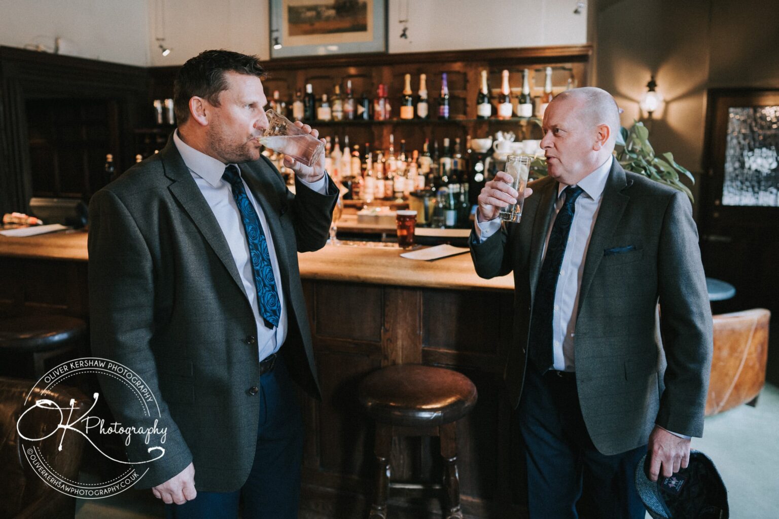 Wedding Photography George Hotel Stamford Two men in suits standing at a bar, drinking from pint glasses.
