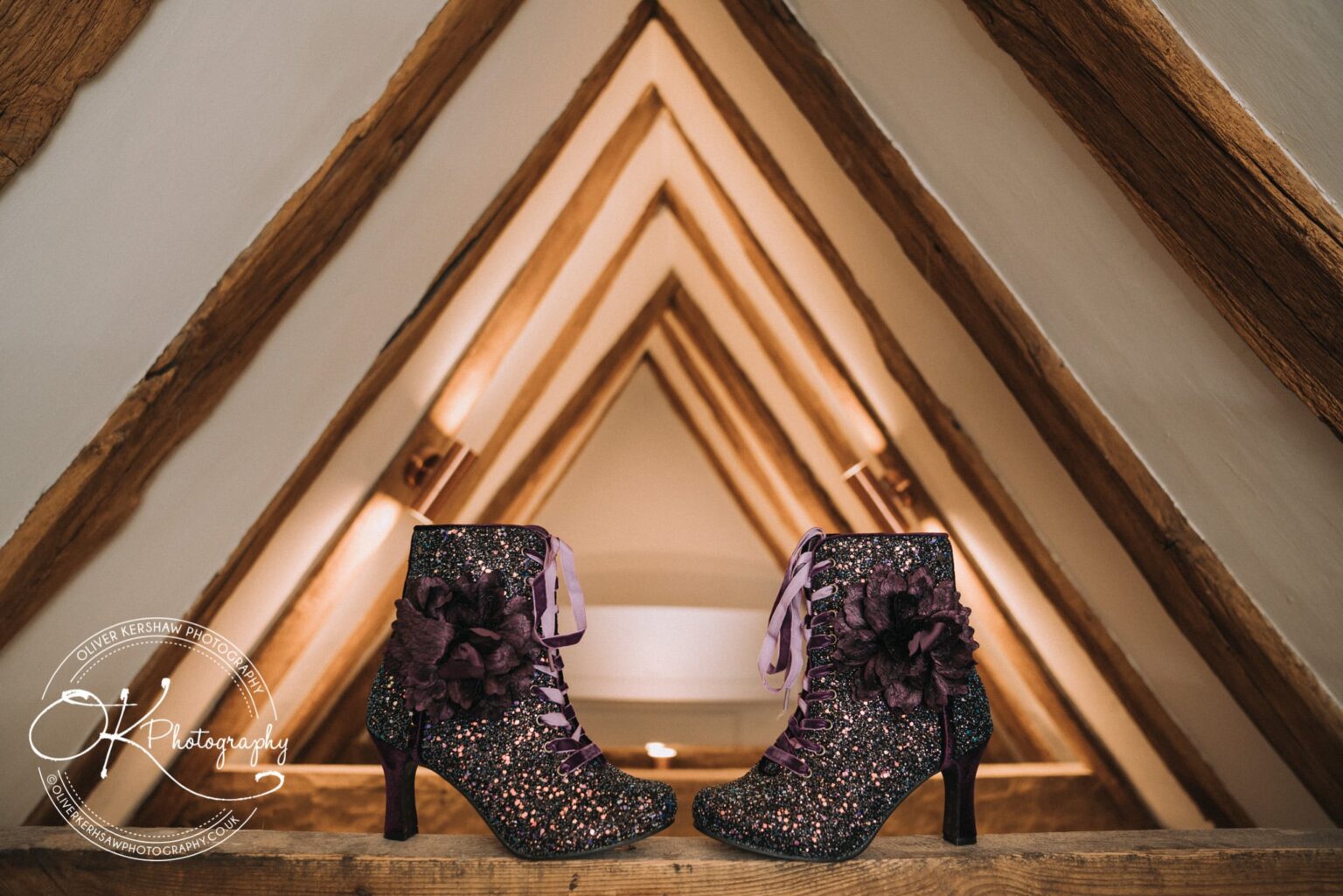 Wedding Photography George Hotel Stamford A pair of sparkly high-heeled boots with purple laces and flower appliqués placed against a backdrop of wooden beams converging towards the ceiling.