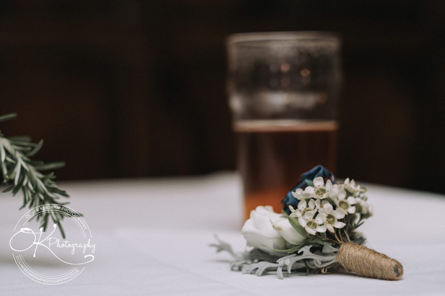 Wedding Photography George Hotel Stamford A pint of amber beer in a glass on a white tablecloth with a boutonniere of white and blue flowers in the foreground.