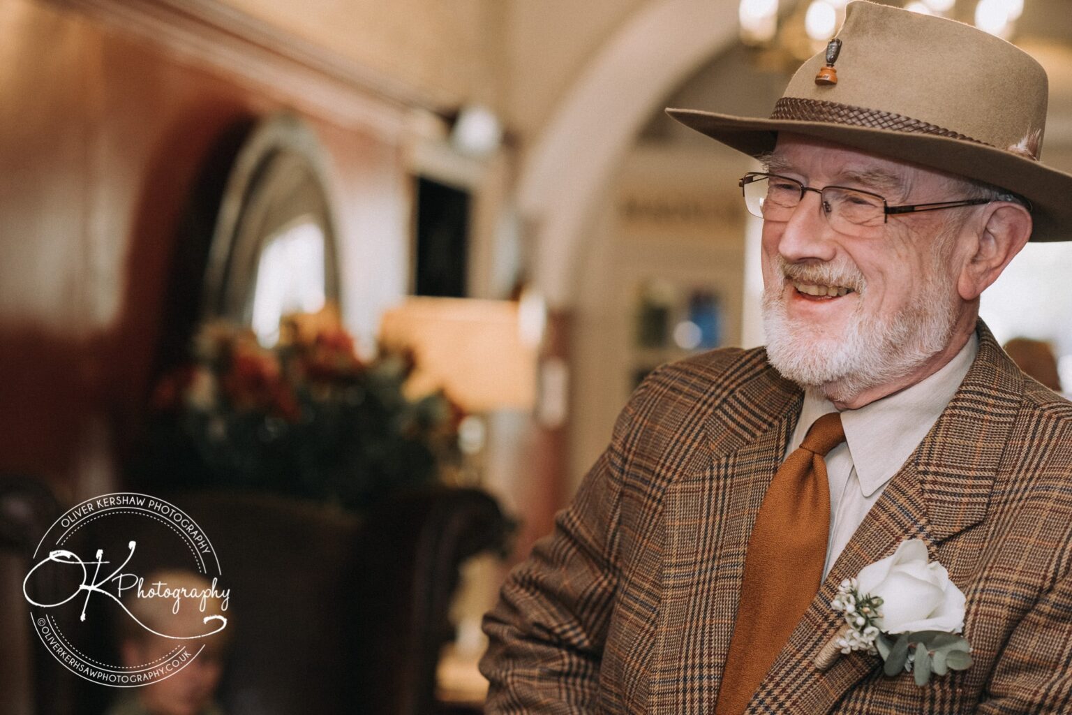 Wedding Photography George Hotel Stamford Elderly man in a plaid suit and hat smiling, with a white boutonnière on his lapel, at the George Hotel in Stamford.