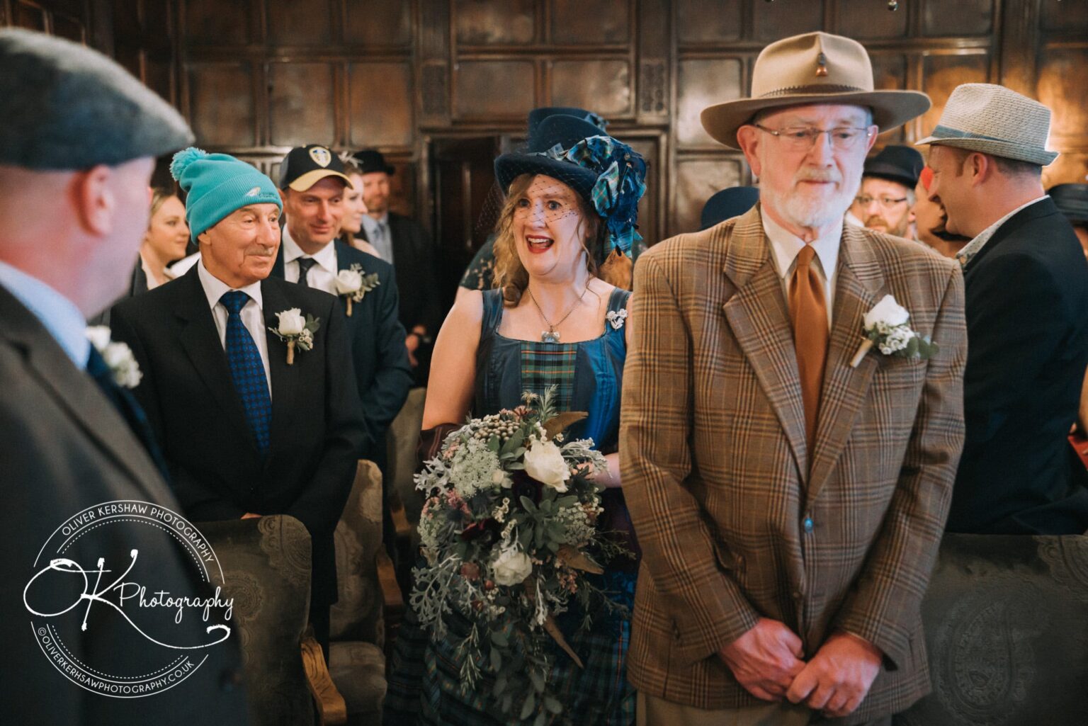 Wedding Photography George Hotel Stamford People in formal attire and a variety of hats, including a woman holding a bouquet, in a wood-panelled room during a gathering at the George Hotel in Stamford.