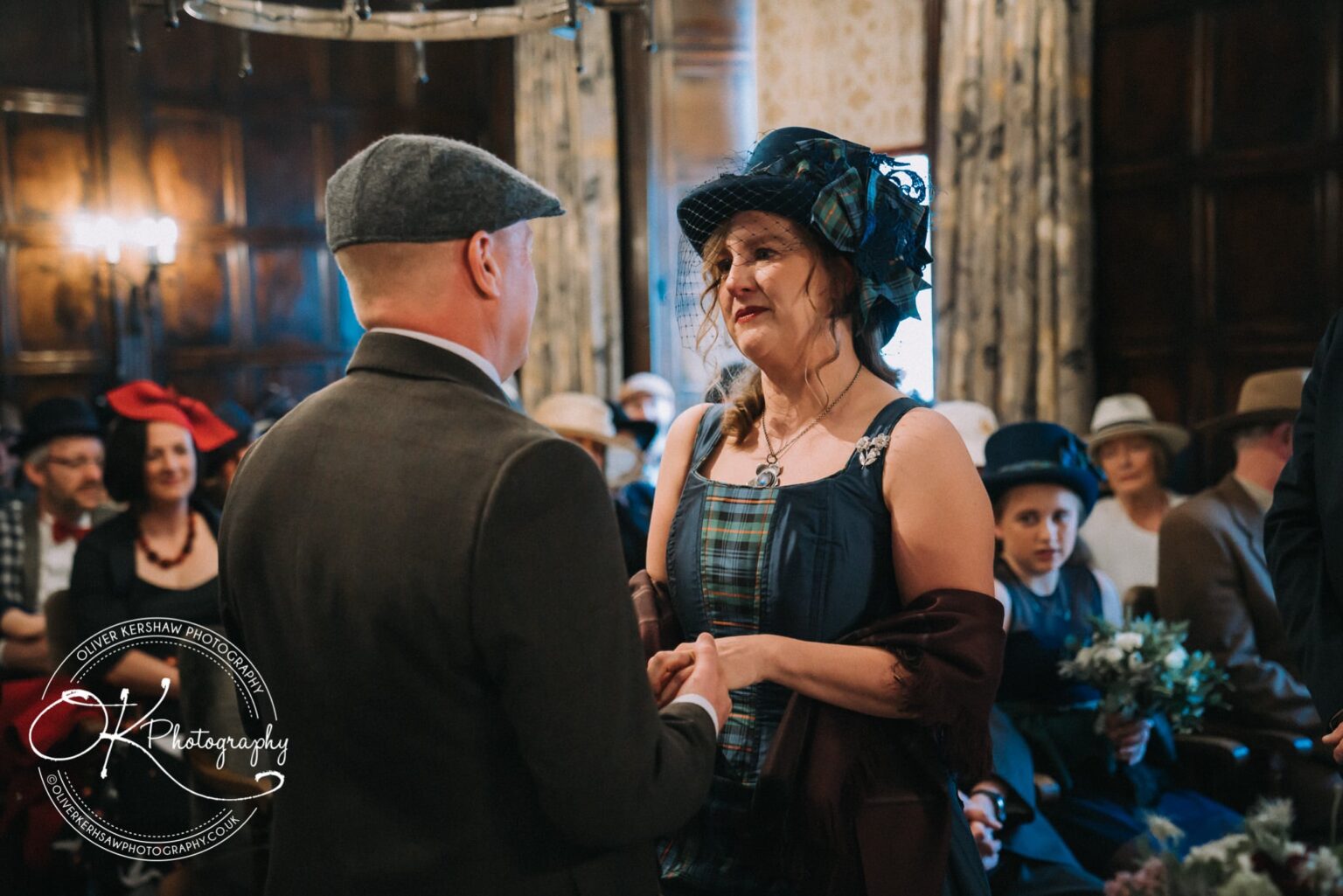 Wedding Photography George Hotel Stamford A couple dressed in vintage attire holding hands, with guests in the background, during a ceremony at George Hotel Stamford.