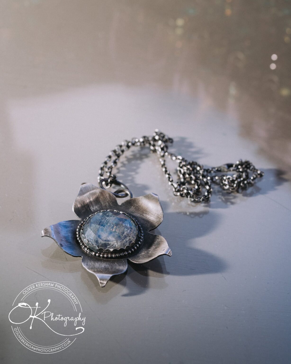 Wedding Photography George Hotel Stamford Silver flower pendant necklace with a blue gemstone on a reflective surface.