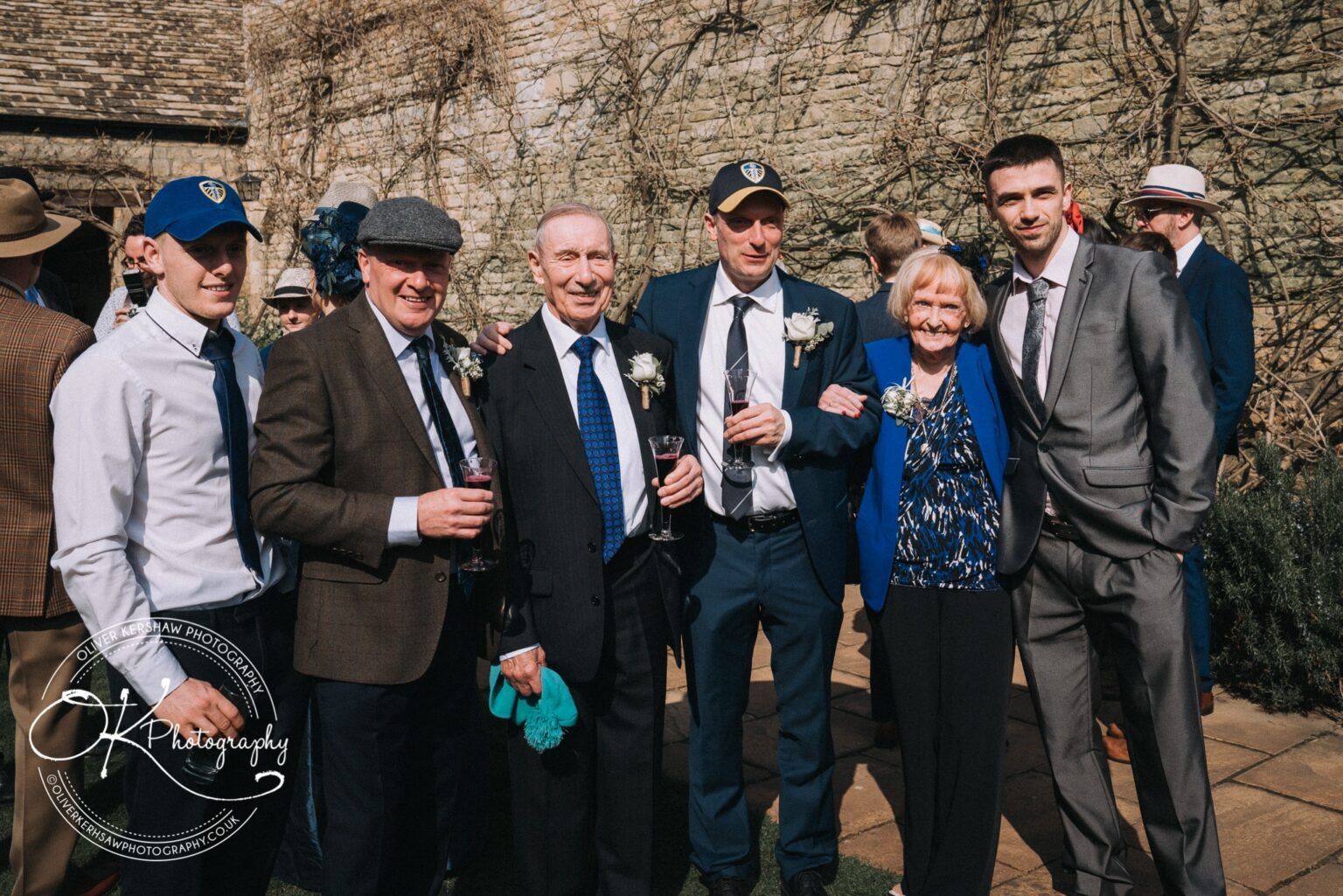 Wedding Photography George Hotel Stamford Group of six people dressed in formal attire posing and holding drinks outside a stone building.