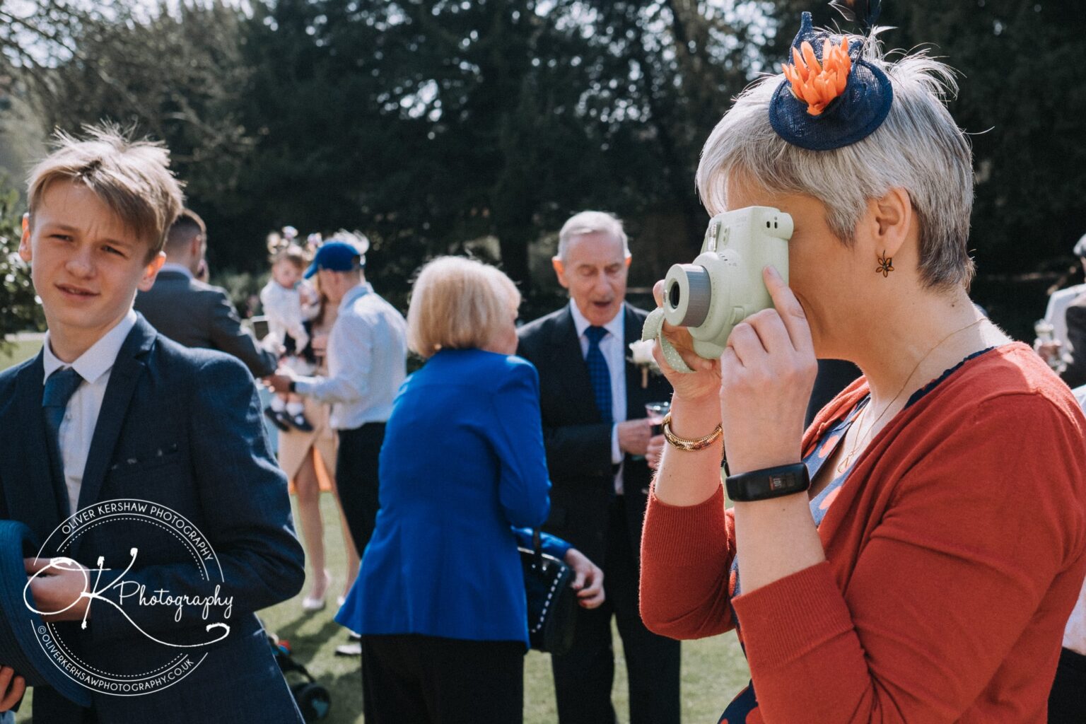 Wedding Photography George Hotel Stamford A woman taking a photo with an instant camera while a group of people, including a young boy and an elderly man, are socialising outdoors.