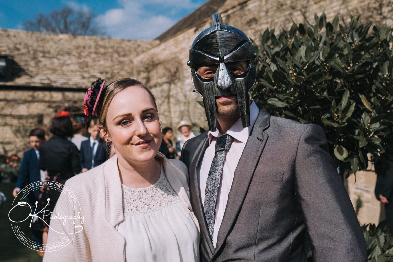 Wedding Photography George Hotel Stamford A woman stands next to a man wearing a medieval-style helmet at an outdoor event.