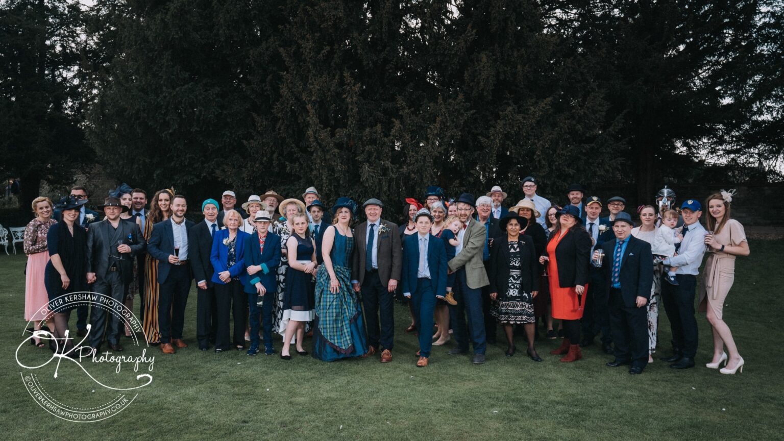 Wedding Photography George Hotel Stamford A large group of people dressed in formal attire standing outside on a lawn, with trees in the background.