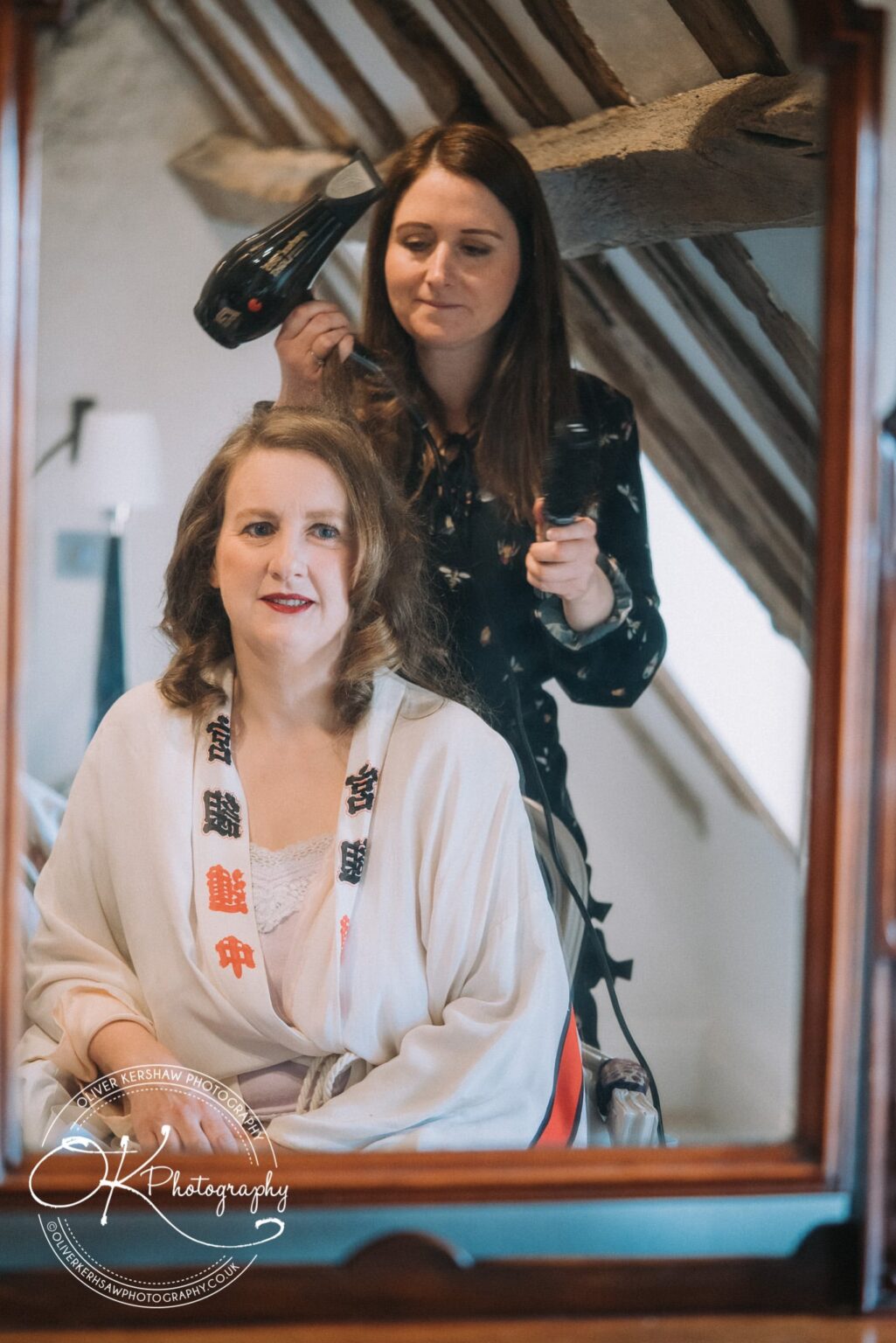 Wedding Photography George Hotel Stamford Woman having her hair styled while seated, reflected in a mirror with wooden beams visible in the background.