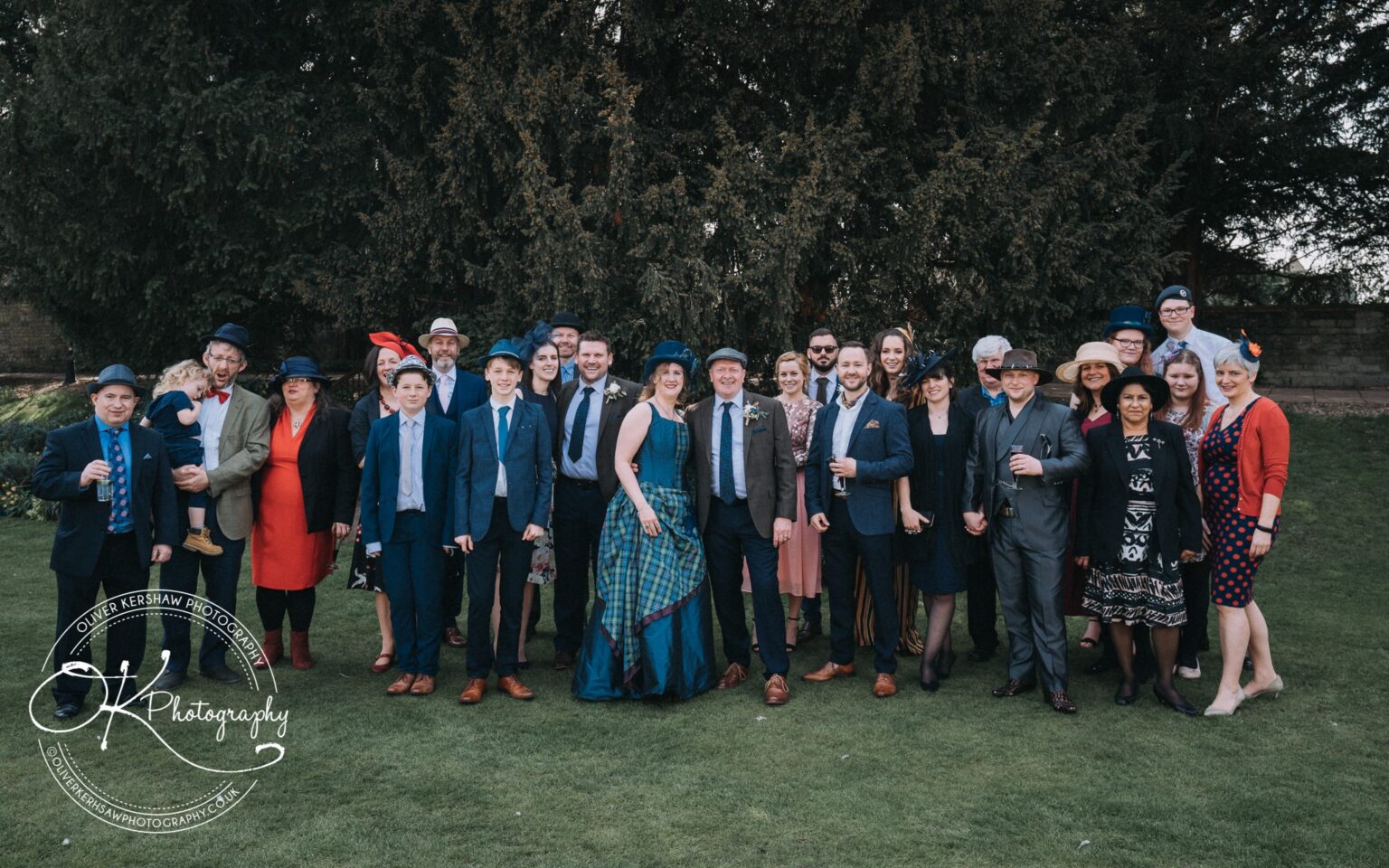 Wedding Photography George Hotel Stamford A group of people dressed in formal attire and hats posing on a lawn outside the George Hotel in Stamford.