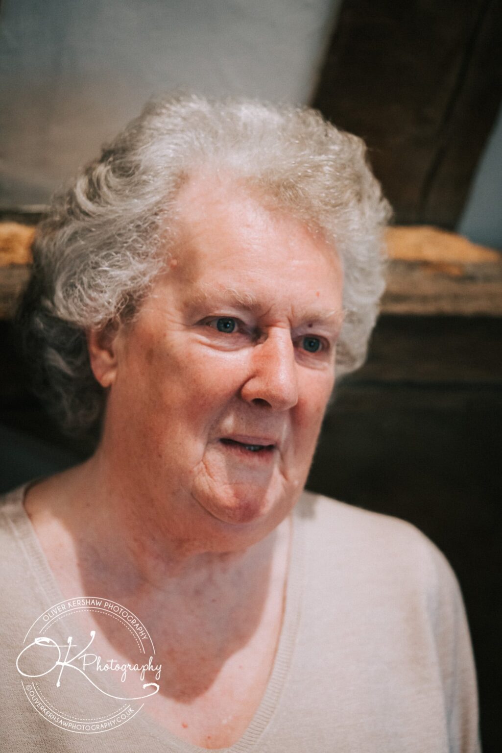 Wedding Photography George Hotel Stamford An elderly person with short, curly grey hair, wearing a light-coloured top and looking slightly to the side.