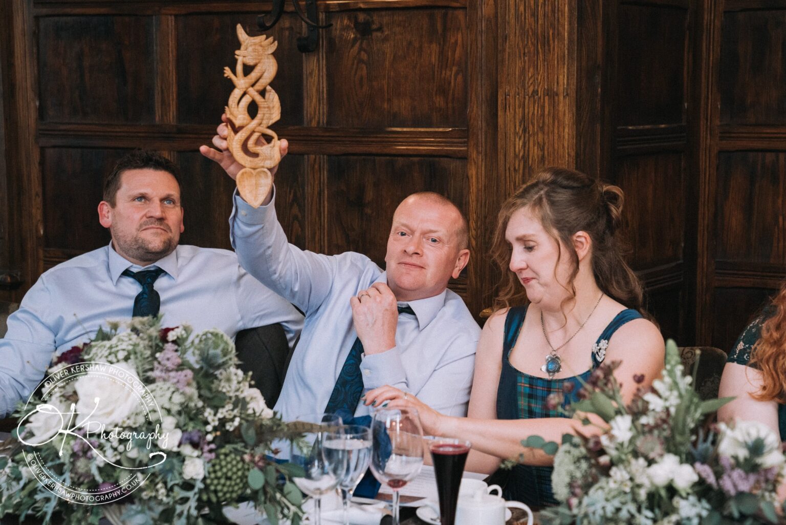 Wedding Photography George Hotel Stamford Three people sitting at a decorated table, with one man holding up a wooden carving.