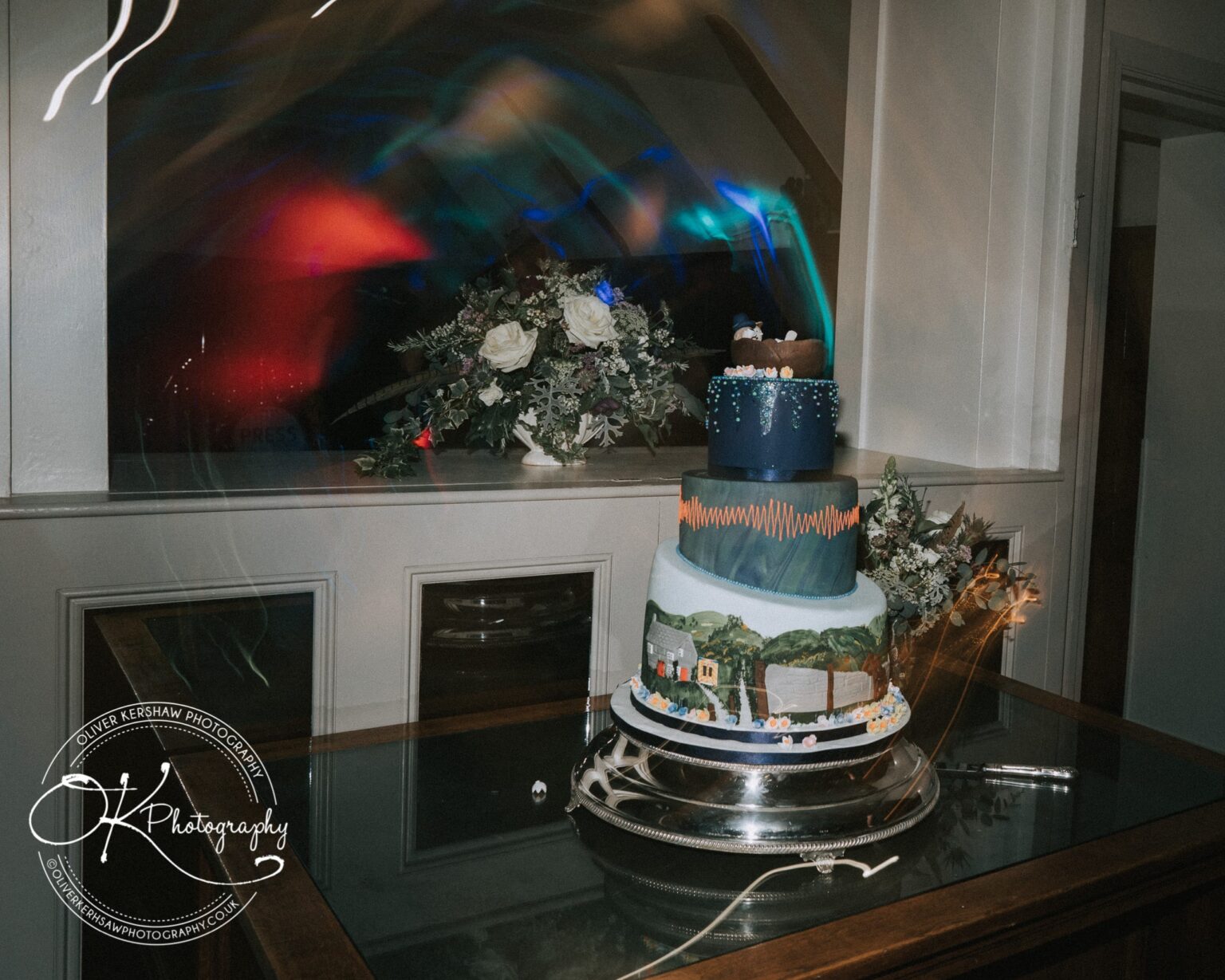Wedding Photography George Hotel Stamford Multi-tiered wedding cake with intricate designs, set on a reflective surface with floral arrangements in the background.