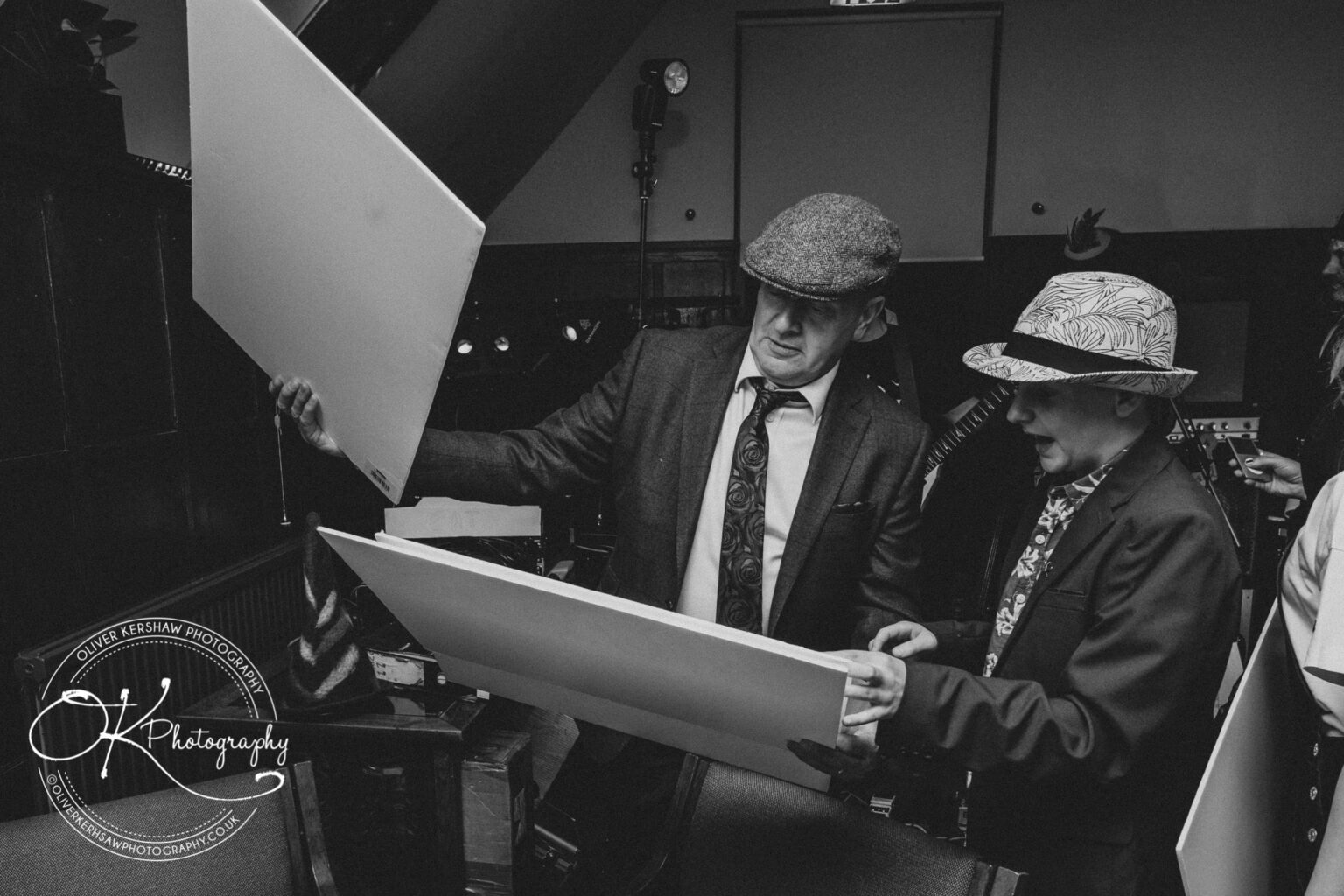 Wedding Photography George Hotel Stamford Two men in suits and hats examining large white boards in a dimly-lit room.
