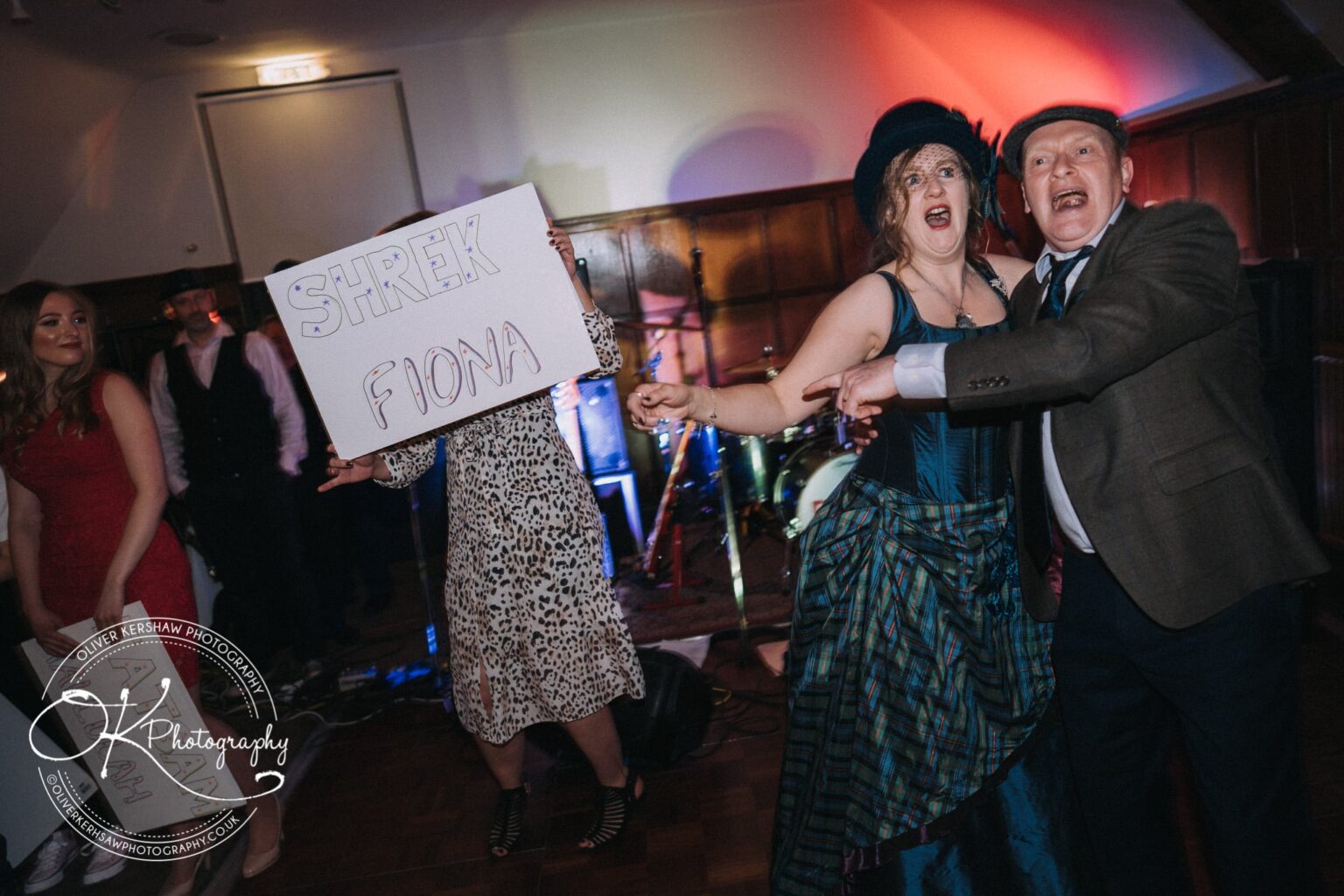 Wedding Photography George Hotel Stamford Two people in costume posing excitedly; another person behind them holding a sign that says "Shrek Fiona" at a party.
