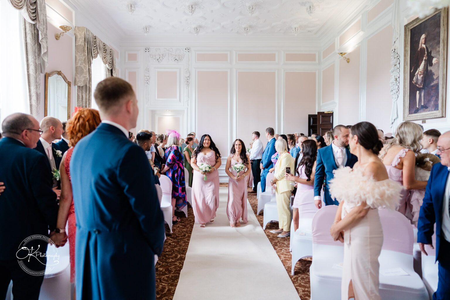 A wedding ceremony at Bosworth Hall Hotel with guests seated and bridesmaids walking down the aisle.