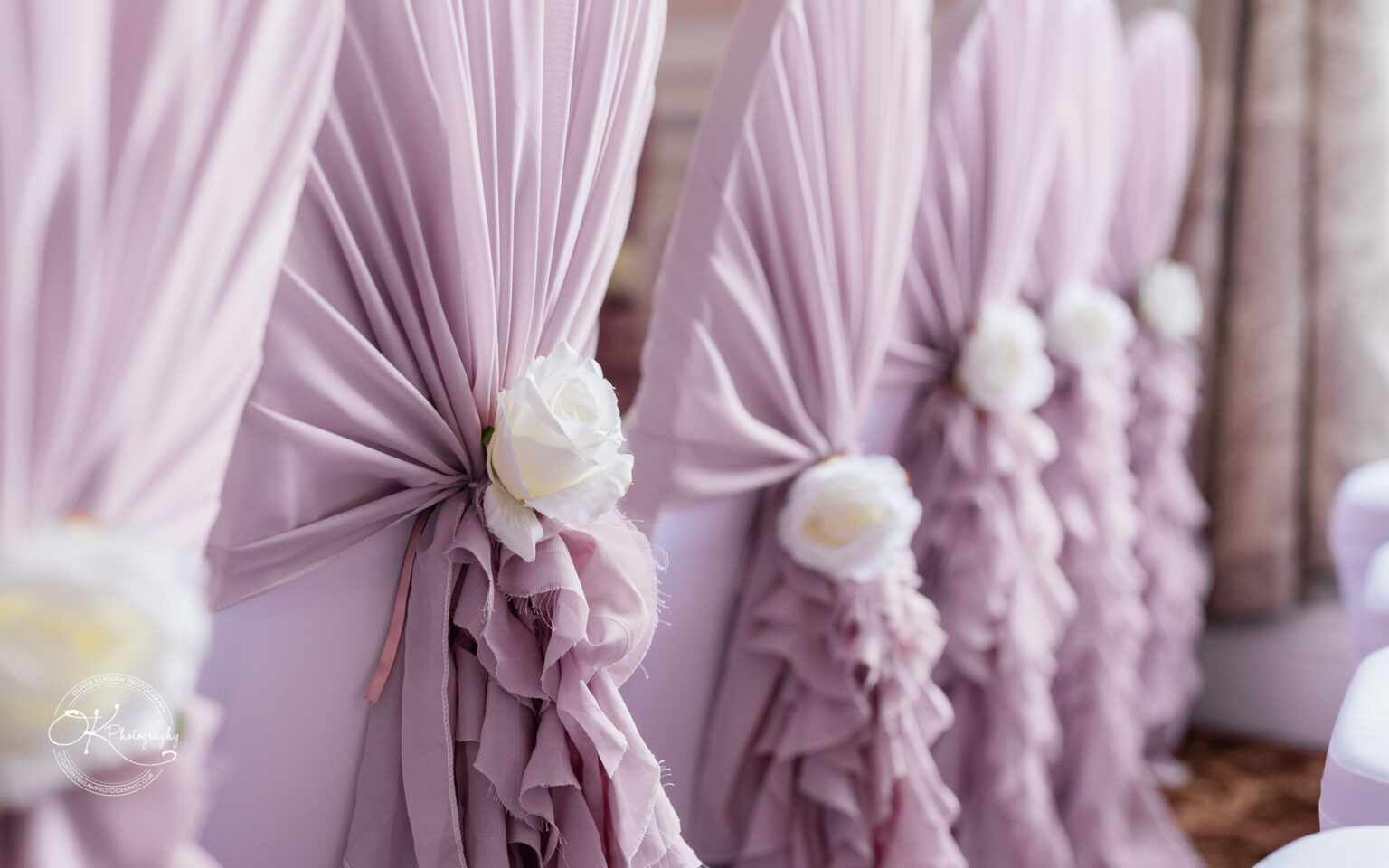 Chairs draped with light pink fabric and decorated with white roses.