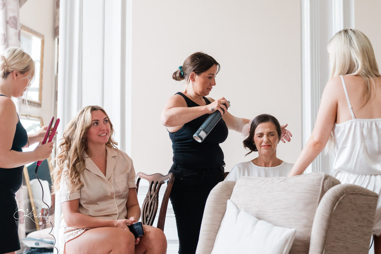 Two women having their hair styled by two hairstylists in a brightly lit room.