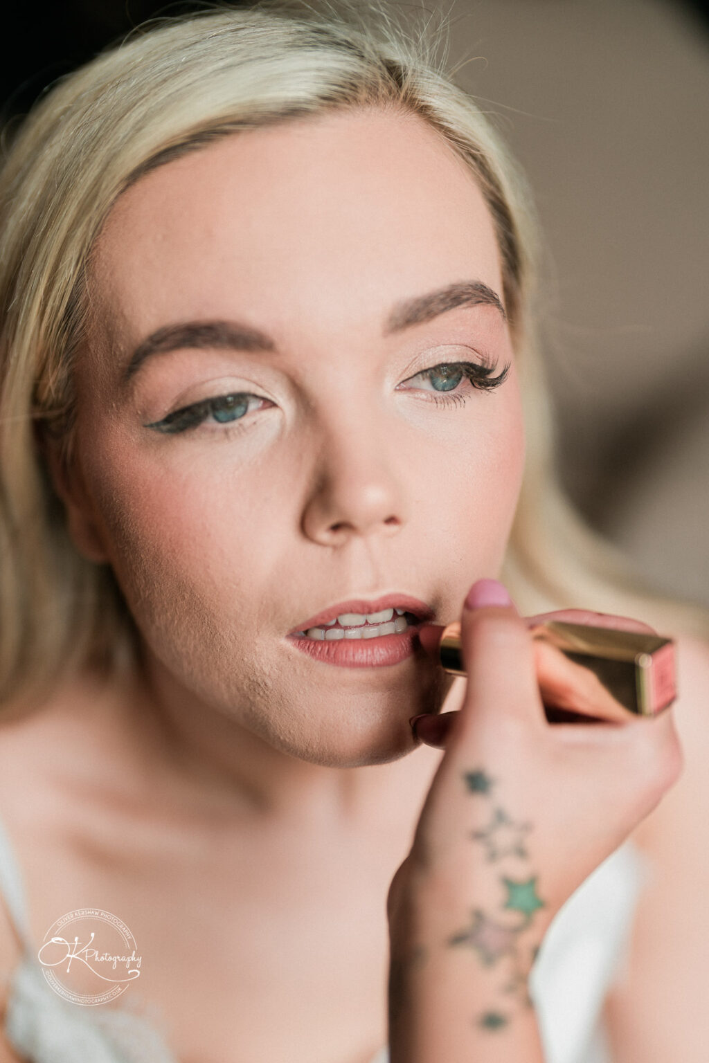 A woman applying lipstick with a hand showing star tattoos in the foreground.