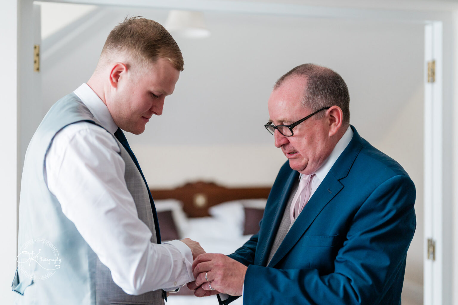 Two men in formal attire, one helping the other with his shirt cuffs.