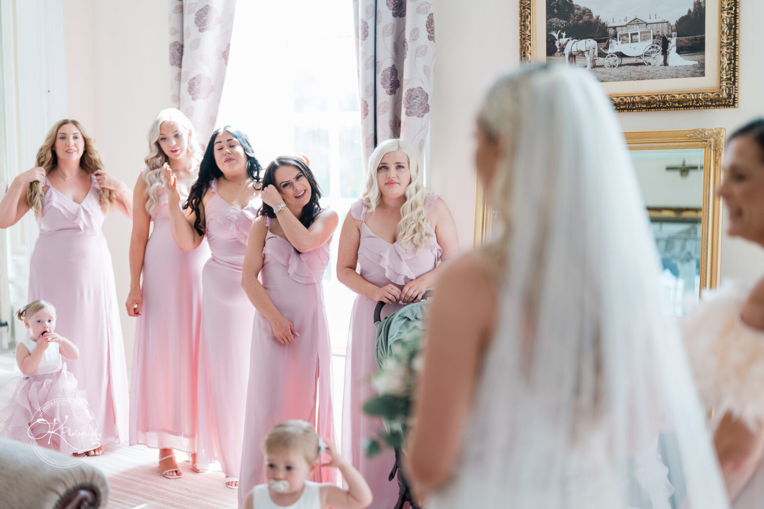 Group of bridesmaids and children in pastel pink dresses, with the bride in a white veil, preparing for a wedding at Bosworth Hall Hotel.